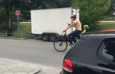 Radfahrer mit Kind an Bord bedient sein Handy während der Fahrt