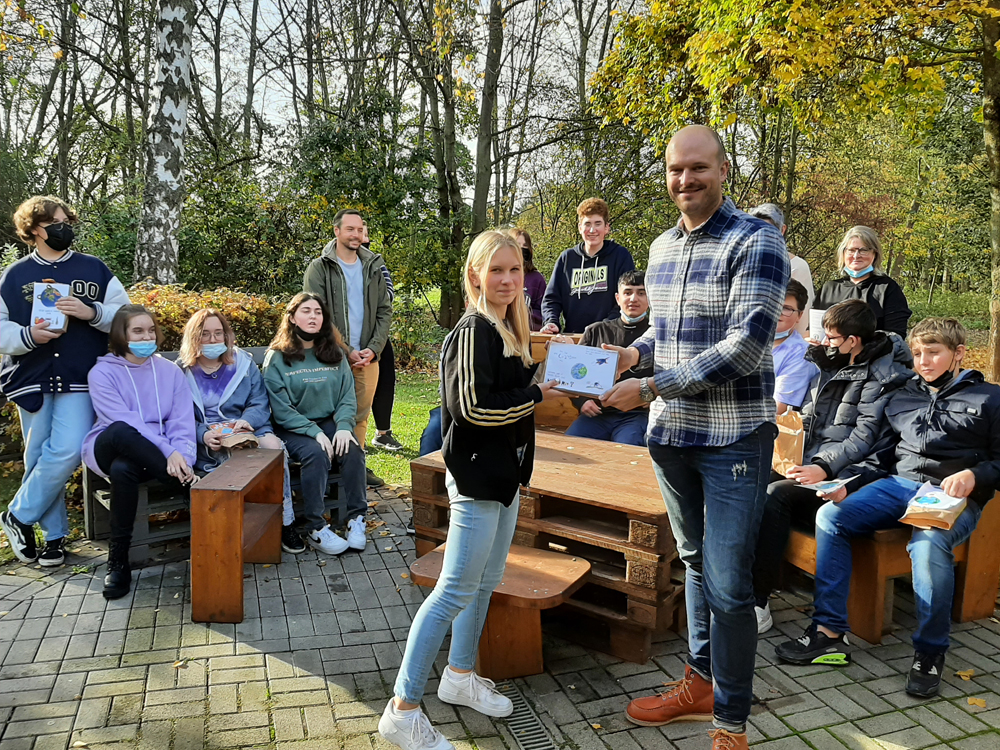 Schüler Jannoübergibt Moritz Mühlen, Geschäftsführer von EMIKO, seine Klimabotschaft„Save the ea (Bi Schüler Jannoübergibt Moritz Mühlen, Geschäftsführer von EMIKO, seine Klimabotschaft„Save the ea (Bi