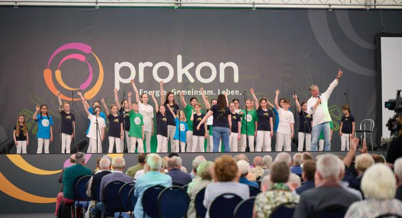 Reinhard Horn mit Chor bei der diesjährigen Jahresversammlung der Energiegenossenschaft Prokon (Bildquelle: Eichinger-Fotografie/Prokon, zum Abdruck frei)
